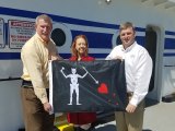 NCDOT Ferry Division Director Harold Thomas, Blackbeard 300 Committee Chair LaRae Umfleet, and Ferry Division Deputy Director Jed Dixon display one of the Blackbeard flags to fly on North Carolina ferries this year.