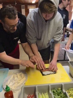 Jason helps a student roll the rice and fillings for sushi.